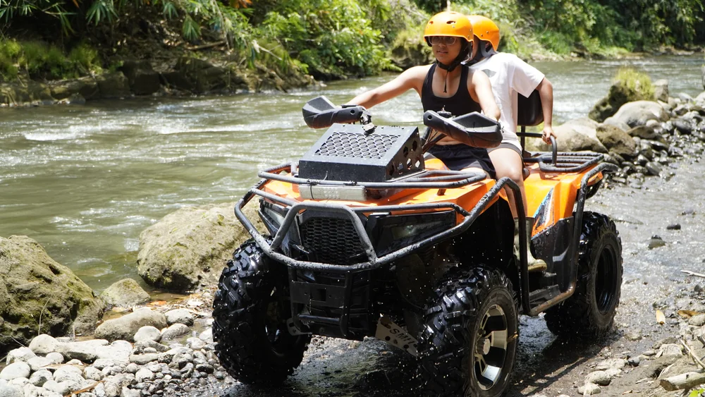Tandem quad bike maneuvering through shallow rocky river rapids
